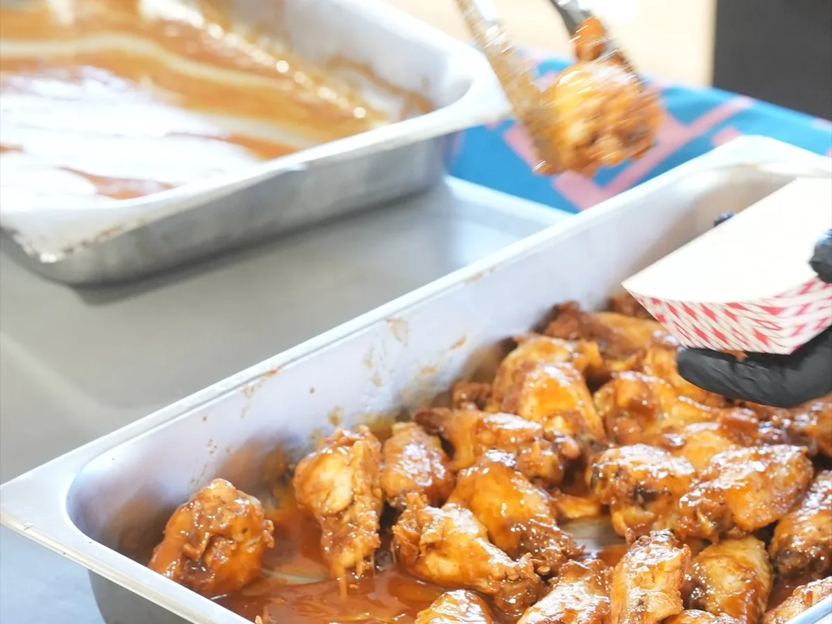 A full hotel pan of freshly sauced chicken wings glistening at a vendor booth