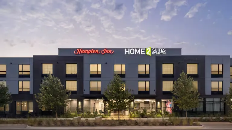 The Hampton Inn and Home2 Suites Austin East Side building at dusk, with both hotel signs lit above the entrance